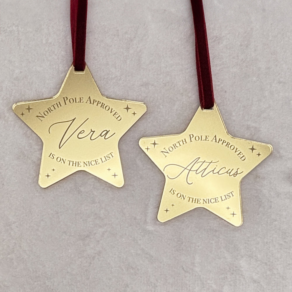 Two gold star-shaped ornaments with names engraved on a gray background