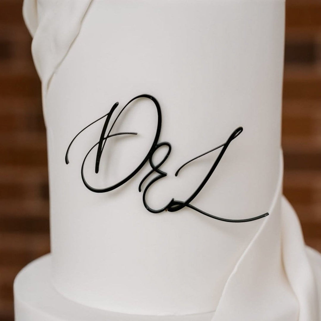White wedding cake with 'D&L' initials against a brick wall background
