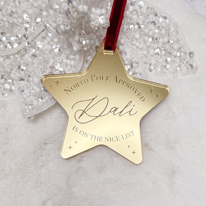 Gold star ornament with 'North Pole Approved Dali is on the Nice List' text on a glittery background