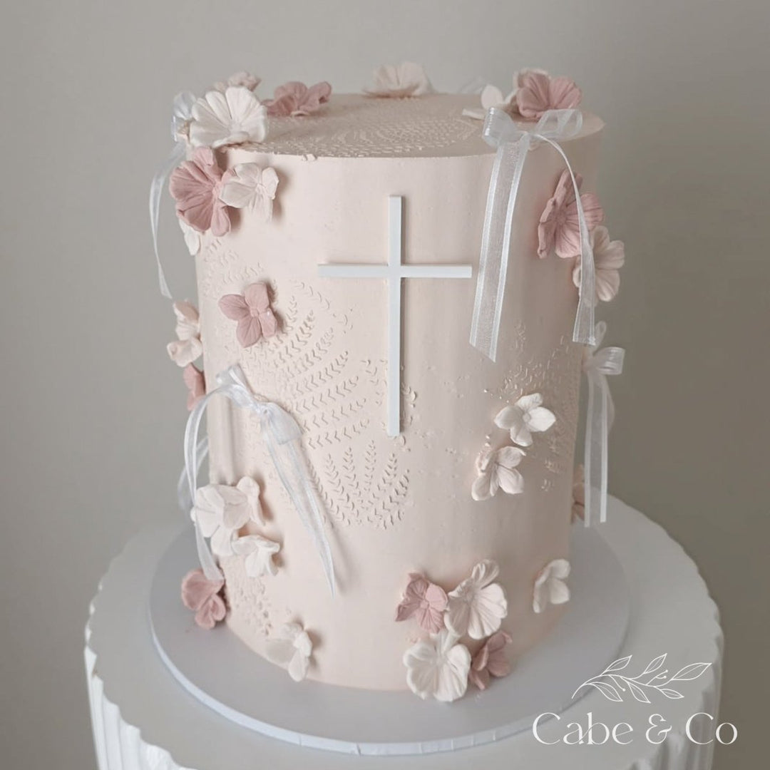 Decorative cake with floral elements and a cross on a plain background