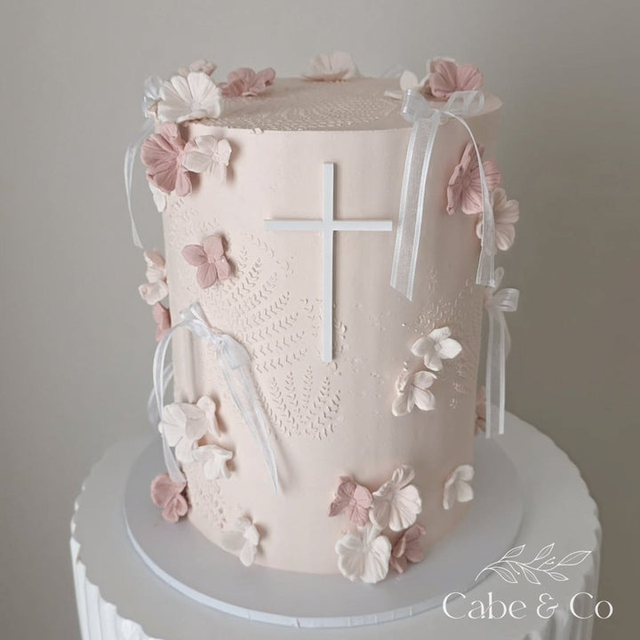 Decorative cake with floral elements and a cross on a plain background